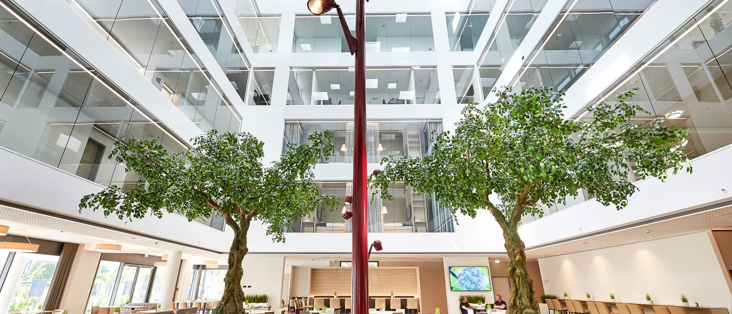 Großzügiger, lichtdurchfluteter Lobbybereich mit Bäumen und modernen Sitzgelegenheiten im Zentrum.
