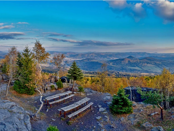 Hoher Schneeberg Zwei Holzbänke auf einem felsigen Aussichtspunkt mit Blick auf bewaldete Hügel und ein Tal unter einem klaren blauen Himmel.