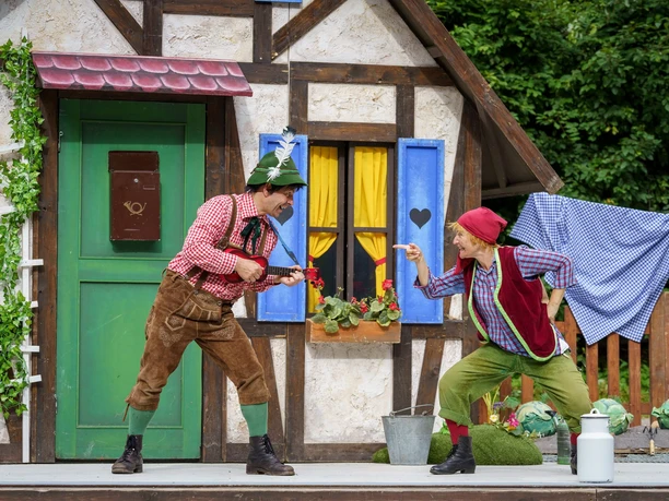 Neues_vom_Räuber_Hotzenplotz_Foto-Dirk-Rückschloss.jpg Zwei Schauspieler in traditioneller Kleidung posieren auf einer Bühne vor einem märchenhaften Haus.