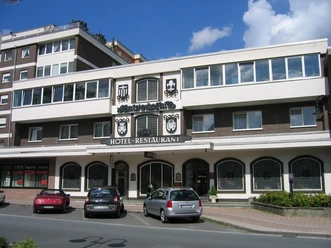 Fassade des dreistöckigen Hotel-Restaurants Kaiserpfalz mit parkenden Autos davor, bei Sonnenschein.