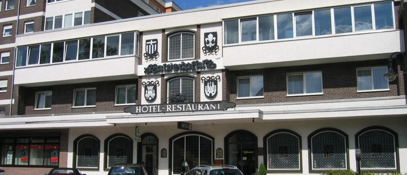 Hotel-Restaurant Kaiserpfalz Fassade des dreistöckigen Hotel-Restaurants Kaiserpfalz mit parkenden Autos davor, bei Sonnenschein.