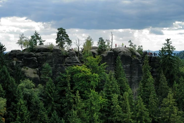 Schauenstein Felsformation mit Bäumen und Menschen auf einem Aussichtspunkt, umgeben von dichtem Wald unter bewölktem Himmel.