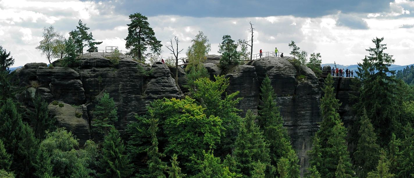 Schauenstein Felsformation mit Bäumen und Menschen auf einem Aussichtspunkt, umgeben von dichtem Wald unter bewölktem Himmel.