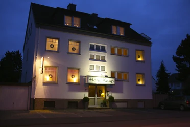 Das Hotel Kaup bei Nacht, beleuchtet und umgeben von Bäumen, mit gut erkennbarer Eingangstür.