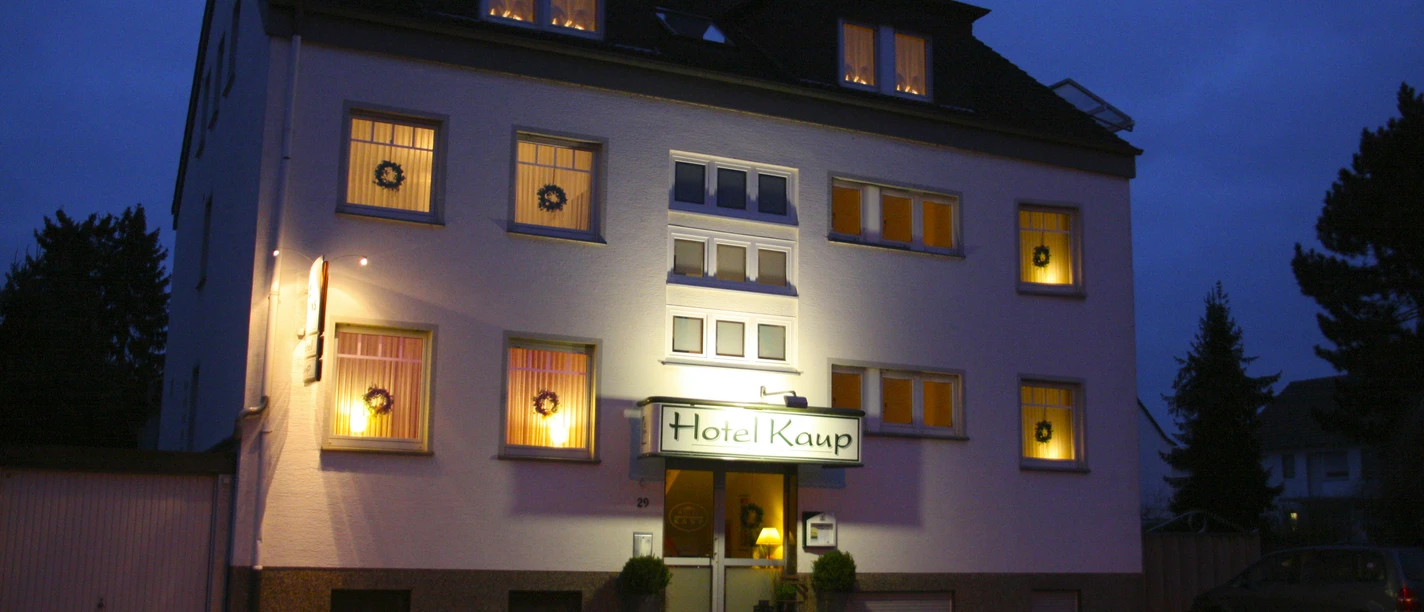 Das Hotel Kaup bei Nacht, beleuchtet und umgeben von Bäumen, mit gut erkennbarer Eingangstür.