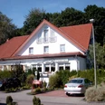 Hotel Restaurant Hubertushof Weißes Gebäude mit rotem Giebeldach, umgeben von Pflanzen, mit Parkplatz und eingangsseitigen Fenstern.