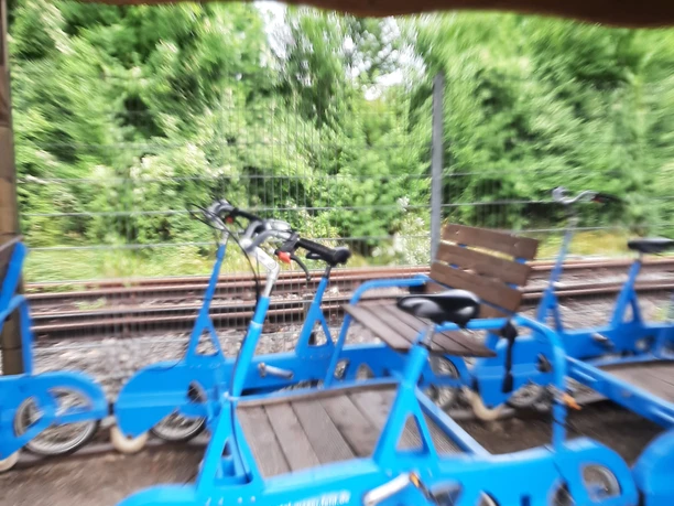 Draisinen Blaue Fahrraddraisinen stehen unter einem überdachten Unterstand an einem von Bäumen gesäumten Gleis.
