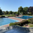 Freibad Rahden Ein Freibad mit zwei Schwimmbecken, umgeben von Rasenflächen und Bäumen an einem sonnigen Tag.