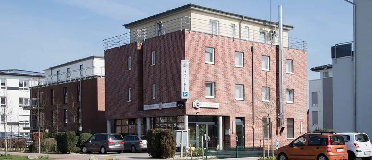 Hotel Manu Dreistöckiges Backsteinhotel mit moderner Architektur, Parkplatz und Eingang auf urbaner Straßenecke.