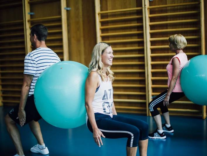 Rückentraing Menschen trainieren in einer Turnhalle mit Gymnastikbällen. Sie sitzen mit den Bällen an der Wand.
