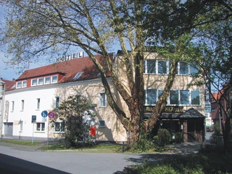 Hotel Cherusker Hof mit hellen Fassaden und markantem Baum im Vordergrund, in einer urbanen Umgebung.