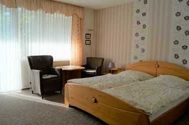 Gästehaus Maahs Helles Schlafzimmer mit zwei Betten, Sitzbereich und Blumentapete, durchflutet von Tageslicht.