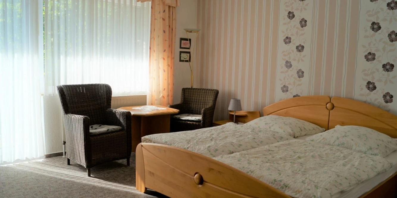 Gästehaus Maahs Helles Schlafzimmer mit zwei Betten, Sitzbereich und Blumentapete, durchflutet von Tageslicht.