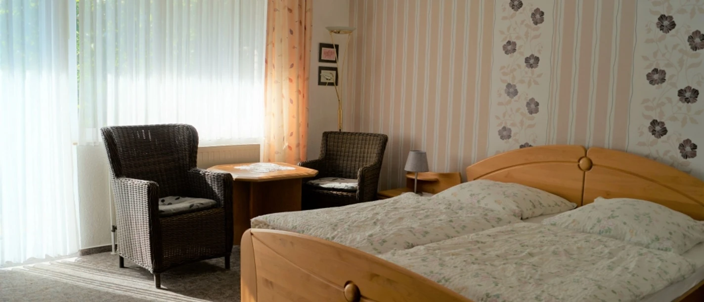 Gästehaus Maahs Helles Schlafzimmer mit zwei Betten, Sitzbereich und Blumentapete, durchflutet von Tageslicht.