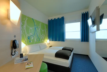 Zweibettzimmer mit modernen Möbeln, blauer Teppich, farbige Akzente und Flachbildfernseher.