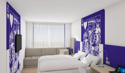 IBB Blue Hotel Paderborn Moderne Hotelzimmer mit Doppelbett, stilvolle Kunst an Wänden, Sofa, Schreibtisch und großem Fenster.