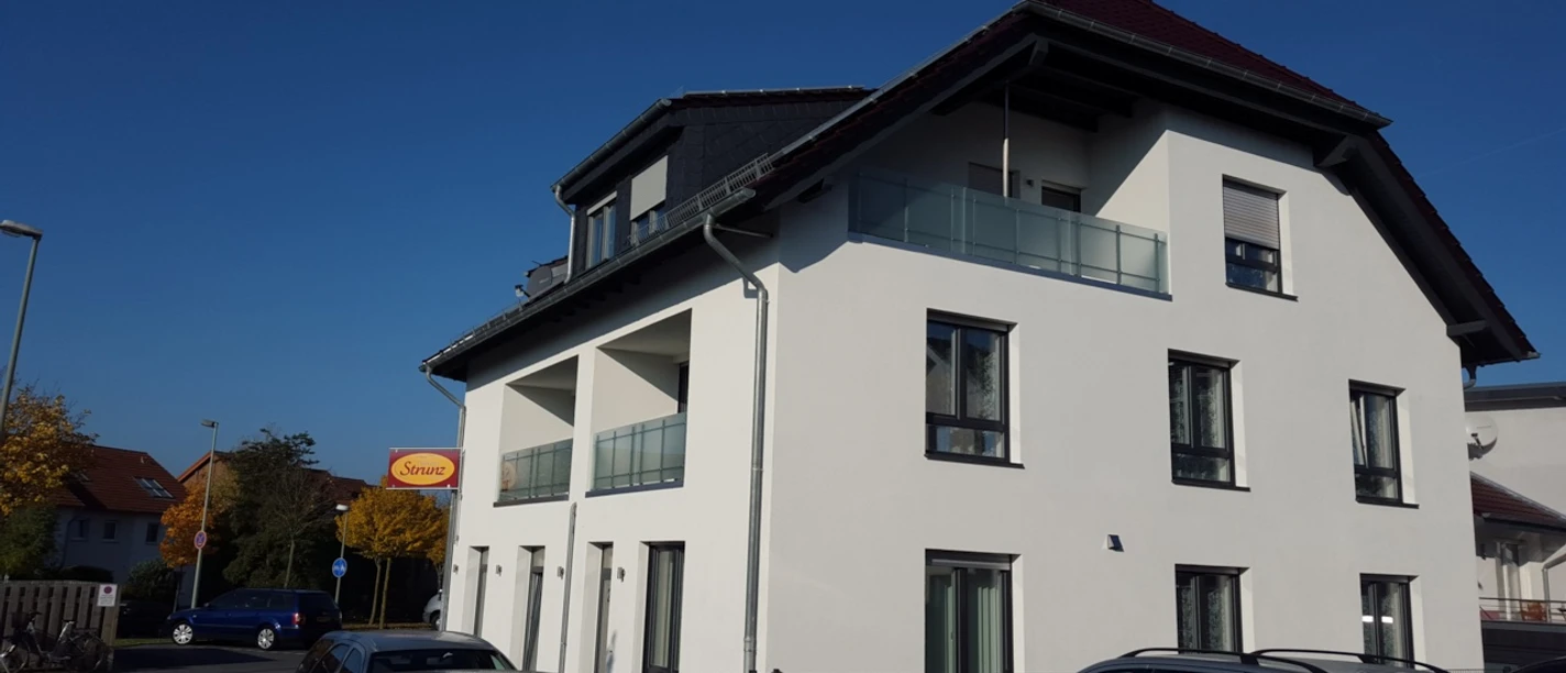 Ein modernes zweistöckiges Gebäude mit weißer Fassade und Balkonen, umgeben von Autos.