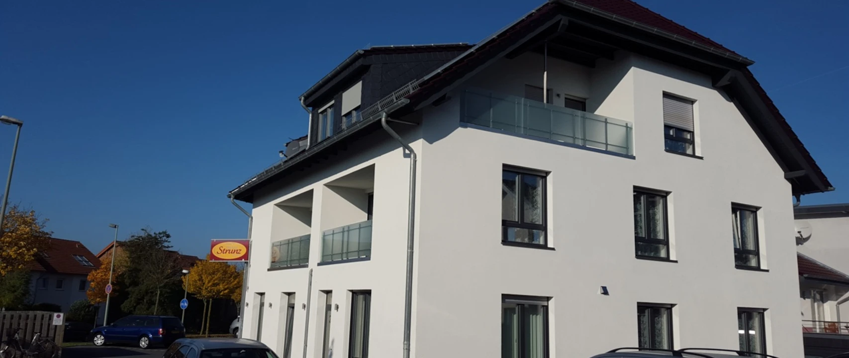 Zimmervermietung Aras Ein modernes zweistöckiges Gebäude mit weißer Fassade und Balkonen, umgeben von Autos.