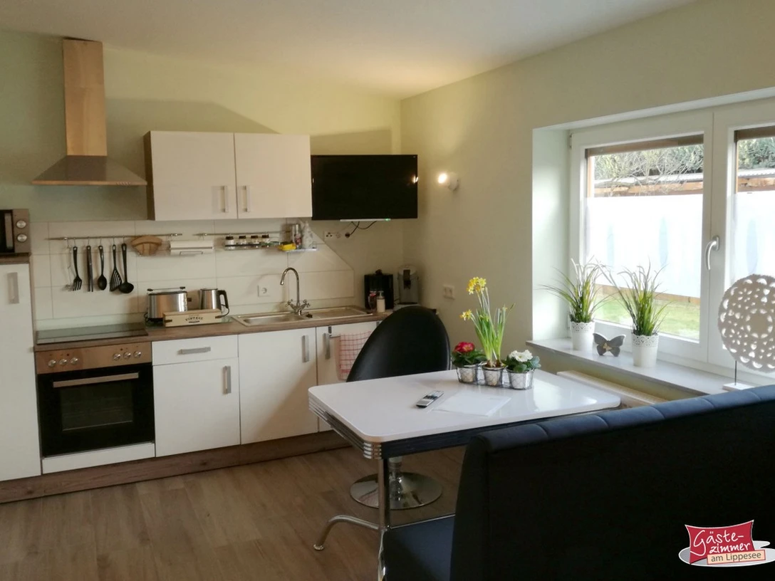 Gästezimmer am Lippesee Moderne Küche in einer Ferienwohnung mit Esstisch, weißen Schränken und Blick auf ein Fenster.