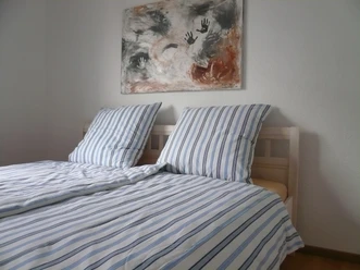 Zweibettzimmer mit gestreifter Bettwäsche, modernem Kunstwerk an weißer Wand, hölzerner Boden.