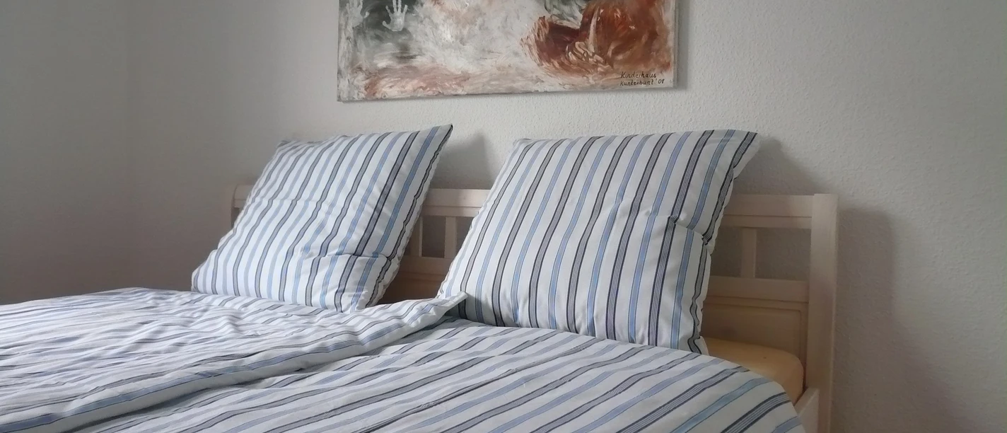 Zweibettzimmer mit gestreifter Bettwäsche, modernem Kunstwerk an weißer Wand, hölzerner Boden.