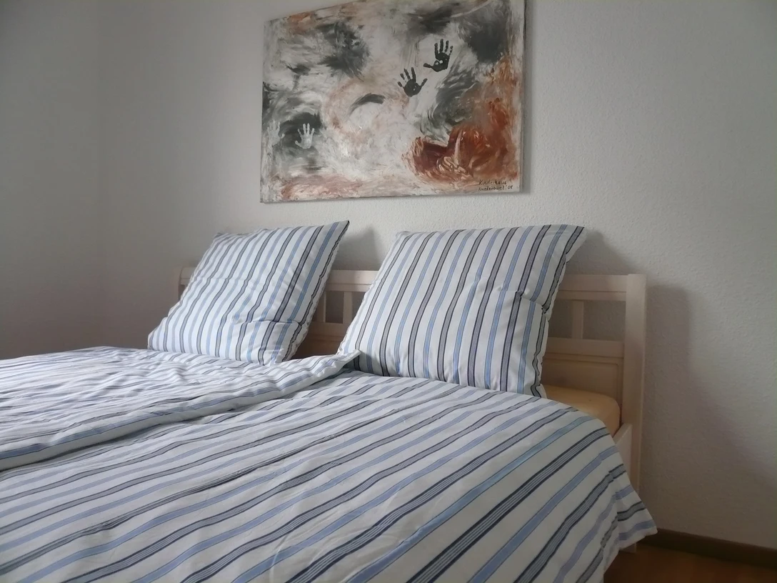 Haus Sofia Zweibettzimmer mit gestreifter Bettwäsche, modernem Kunstwerk an weißer Wand, hölzerner Boden.