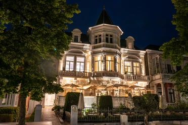 Villa Q Außenansicht Die Villa Q leuchtet in der Nacht. Ihre Architektur wird durch gezielte Beleuchtung hervorgehoben, was sie zu einem auffälligen Anblick macht.