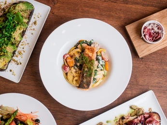 Villa Q Das Bild präsentiert ein angerichtetes Lachsgericht. Neben dem Hauptgericht sind weitere köstliche Speisen und kleine Leckereien platziert, die das Gesamtbild abrunden.