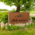 Holzhausen II Schild mit der Aufschrift "Alte Schmiede" vor einer grünen Landschaft mit Baum und Feld im Hintergrund.
