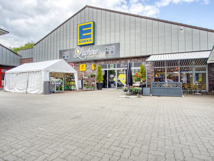 Die Außenansicht des Edeka-Marktes in Lüchow zeigt einen weitläufigen Parkplatz vor einem modernen Ladengebäude. Das flache Dach und die großen Glasfenster prägen das Erscheinungsbild.