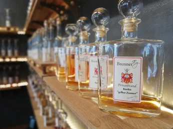 Flaschen mit verschiedenen Spirituosen auf Holzregalen, beschriftet mit "BrennerEy" und Geschmacksrichtungen.