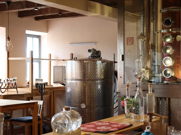 Kupferne Brennblase und Edelstahltank in einer modernen Destillerie, umgeben von Holztischen.