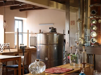 BrennerEy Kupferne Brennblase und Edelstahltank in einer modernen Destillerie, umgeben von Holztischen.