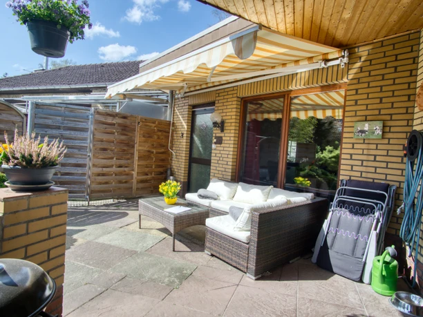 Außenansicht Sonnige Terrasse am Klinkerhaus mit Markise, Rattan-Loungemöbeln und Kugelgrill.