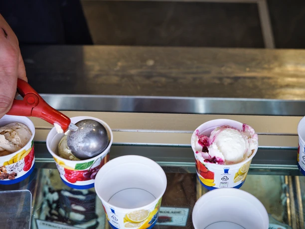 eis-amelinghausen-2022 Ein Eisverkäufer befüllt mit einem Portionierer bunte Pappbecher mit verschiedenen Eissorten.