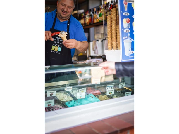 eis-amelinghausen-2022-9.jpg Ein Mann in blauer Arbeitskleidung füllt hinter der Vitrine eine Waffel mit Eiscreme.
