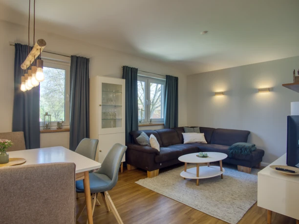 Wohnzimmer Wohnzimmer mit dunklem Ecksofa, weißem Couchtisch, Fernseher und Essplatz mit Stühlen.