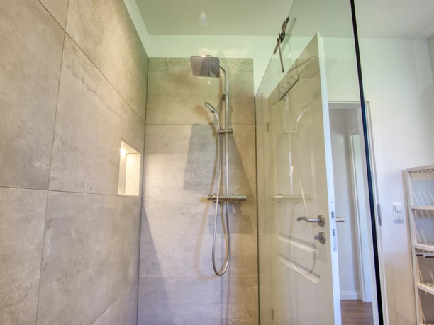 Badezimmer Helles Badezimmer mit moderner Regendusche, grauen Fliesen und einer Trennwand aus Glas.