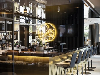 Bar Hotel WunnersWat.jpg Moderne Hotelbar mit eleganter Einrichtung, stilvolle Sitzgelegenheiten und einleuchtendes Neonzeichen.