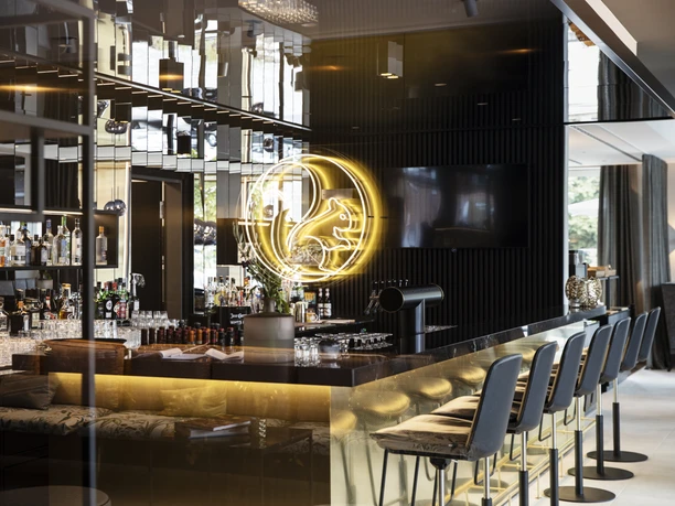 Bar Hotel WunnersWat.jpg Moderne Hotelbar mit eleganter Einrichtung, stilvolle Sitzgelegenheiten und einleuchtendes Neonzeichen.