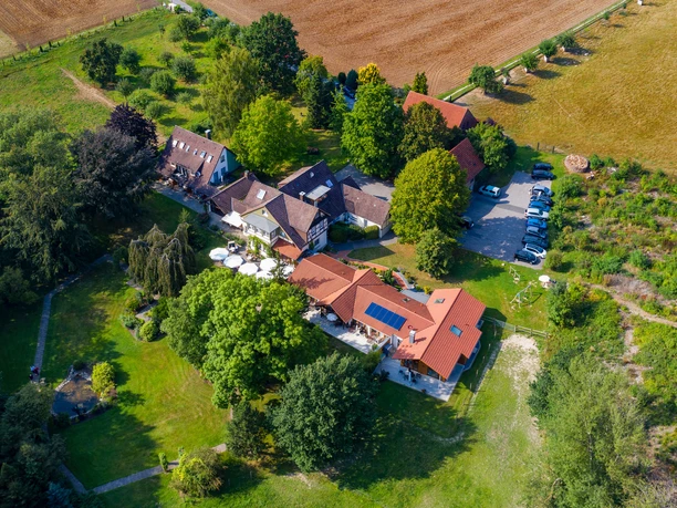 Haus_Berkenkamp.jpg Luftaufnahme eines großen Anwesens mit roten Dächern, umgeben von üppigem Grün und anliegenden Feldern.