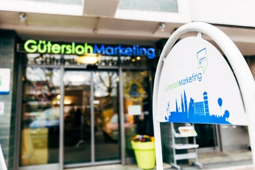 ServiceCenter der Gütersloh Marketing GmbH Eingangsbereich von Gütersloh Marketing mit modernem Logo und stilisierter Stadt-Silhouette auf Schild.