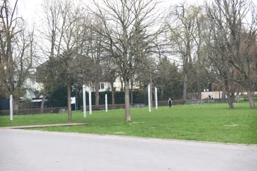IMG_0112.JPG Offener Park mit kahlen Bäumen im Herbst, gepflasterter Weg und eine Person im Hintergrund.