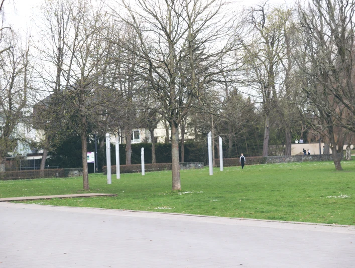 IMG_0112.JPG Offener Park mit kahlen Bäumen im Herbst, gepflasterter Weg und eine Person im Hintergrund.