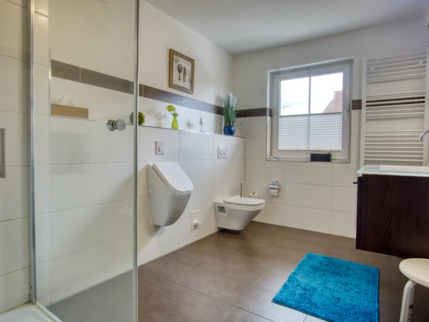 Badezimmer Helles, modern gefliestes Badezimmer mit Glasdusche, Urinal, Toilette und Waschtisch.