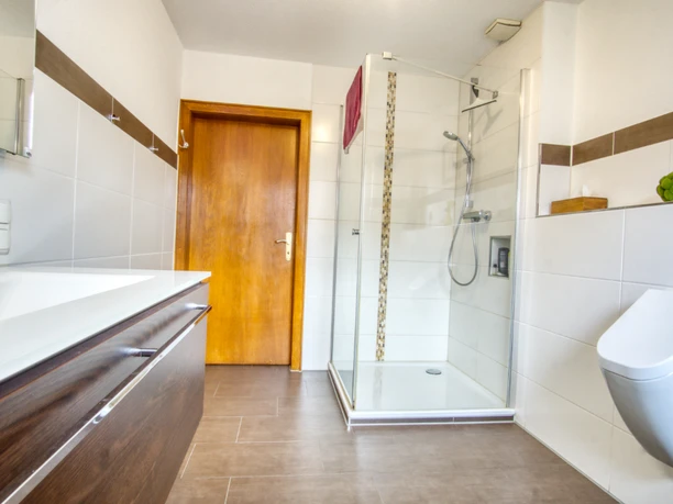 Badezimmer Helles Badezimmer mit Glasdusche, Holzwaschtisch, Urinal und weißen Fliesen.