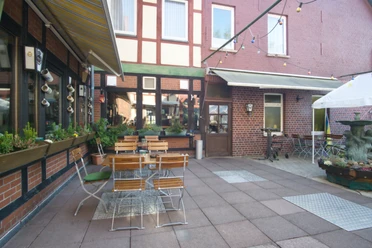 Biergarten Innenhof mit Sitzgelegenheiten, Tischen und einem kleinen Brunnen vor einer Backsteinfassade.