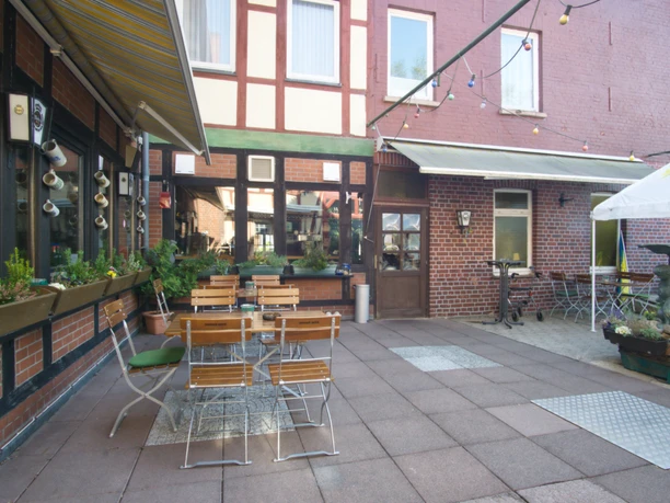 Biergarten Innenhof mit Sitzgelegenheiten, Tischen und einem kleinen Brunnen vor einer Backsteinfassade.