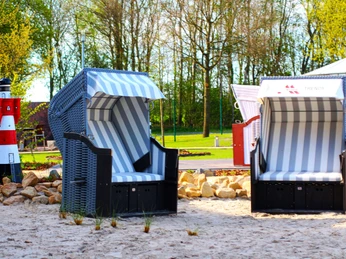 Ausstellung der Strandkörbe Zwei blau-weiß gestreifte Strandkörbe auf Sandfläche neben kleinem rot-weißen Leuchtturmmodell.