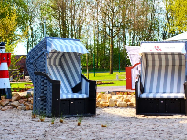 Ausstellung der Strandkörbe Zwei blau-weiß gestreifte Strandkörbe auf Sandfläche neben kleinem rot-weißen Leuchtturmmodell.